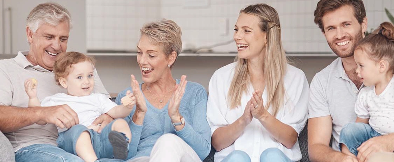 Multigenerational family sitting on couch, smiling. Two kids and four adults.