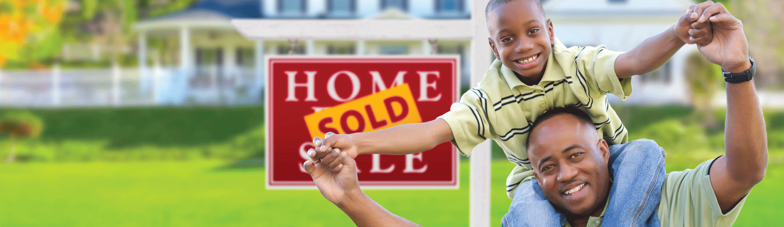 Father and son smiling in front of a home sold sign.