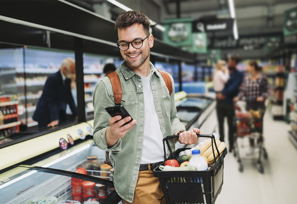 young man grocery shopping looking at his smartphone